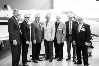 7 men in suits stand in front of a plane