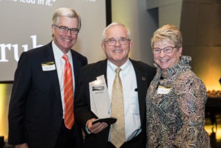 Two Men and a woman pose with metal award.