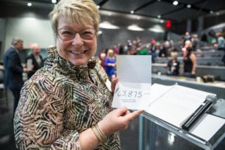 Woman holds a card with number $63,875 written on it