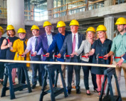 Group of people with hammers and hardhats standing behind a board in an empty building