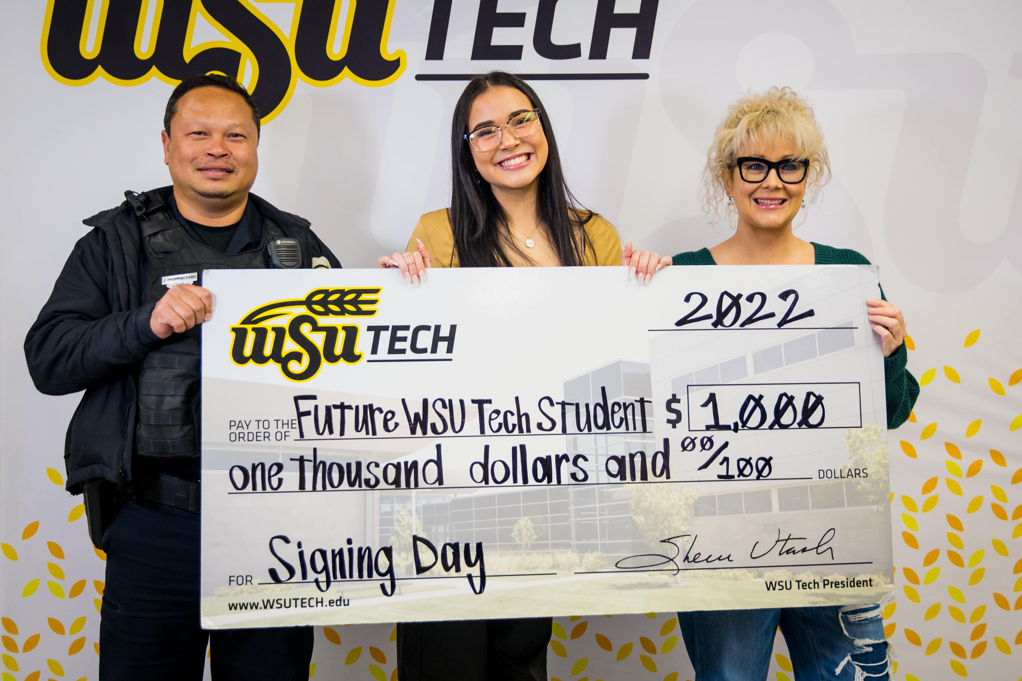 young girl with mom and dad holding an oversized check in front of wsu tech background