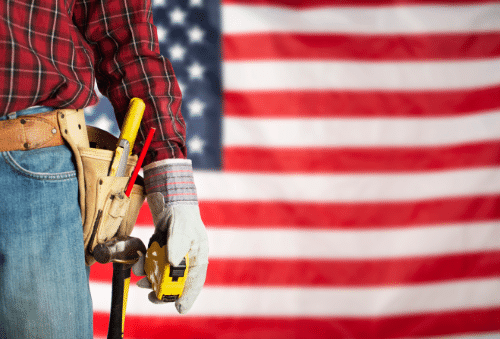 fa-landing-sm-tile-images-2 WSU Tech Veteran and Military Services student support - A construction worker wearing gloves and a tool belt with tools, standing in front of a large American flag.