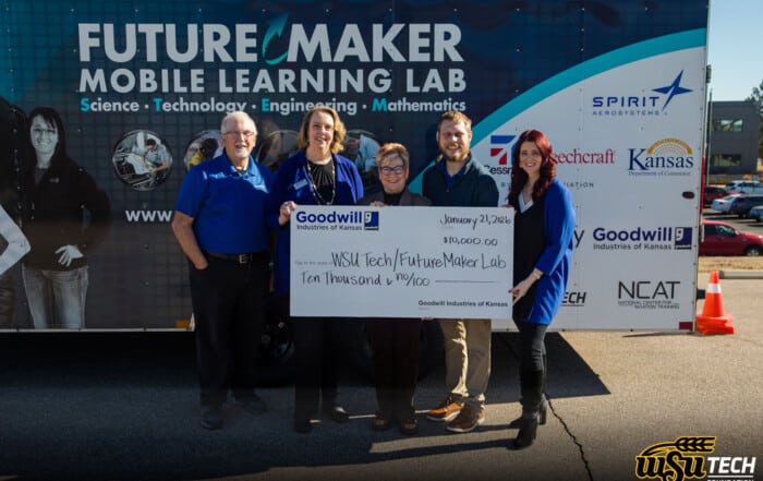 WSU Tech and GoodWill Kansas team members stand in front of FutureMaker Mobile Learning Lab trailer holding a big check for $10k.