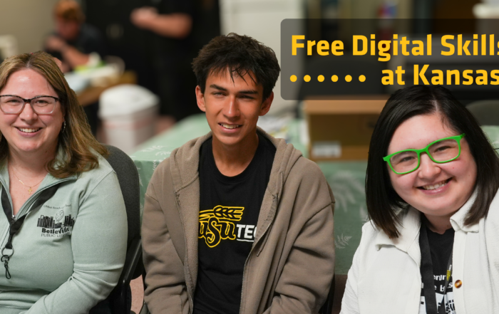 Three individuals are seated and smiling at the camera. The person on the left wears glasses and a light green long-sleeved shirt. The person in the middle wears a brown hoodie over a black t-shirt. The person on the right wears bright green glasses and a white jacket. Text on screen says Free Digital Skills Training at Kansas Libraries