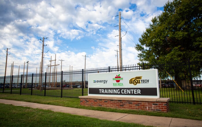 Electric Power Distribution training pole farm at WSU Tech’s City Center campus, featuring rows of wooden utility poles and overhead power lines behind a sign displaying the Evergy, Wichita Public Schools, and WSU Tech logos.