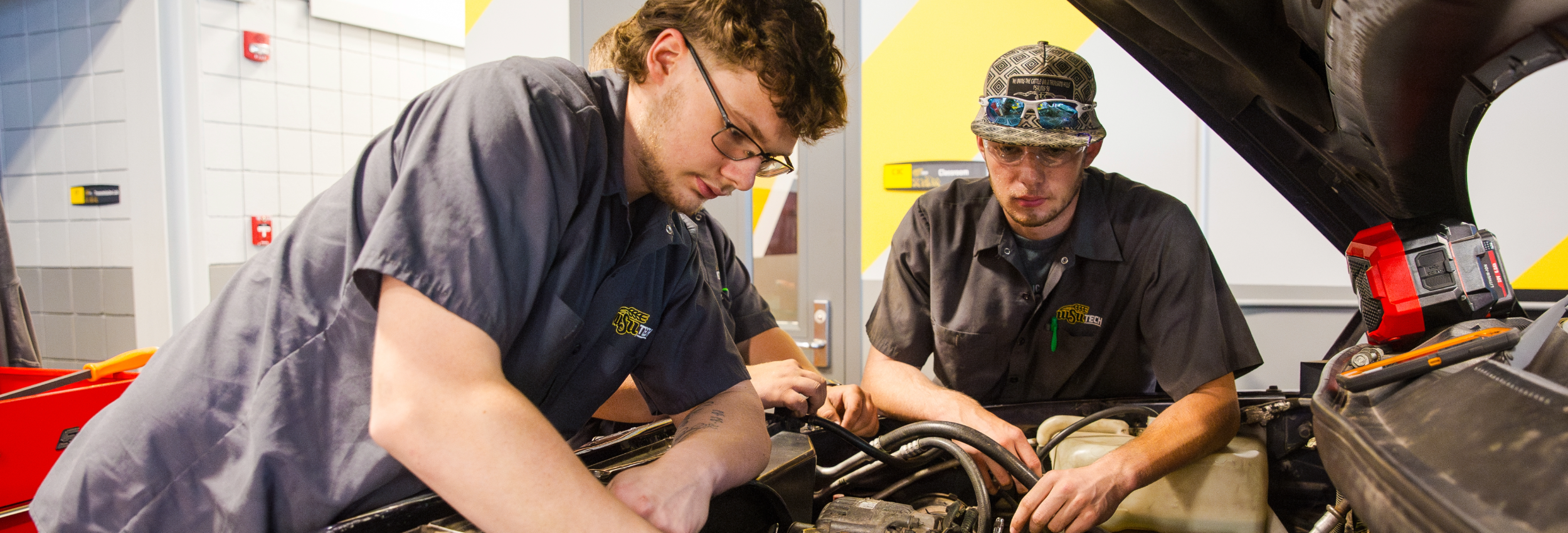 Two WSU Tech automotive students working together under the hood of a vehicle in a training lab.