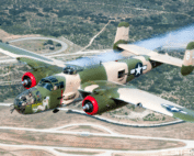 The B-25 Mitchell bomber “Yellow Rose” flies over a landscape with winding roads. The historic World War II aircraft features green and tan camouflage, U.S. military insignia, bright red engine cowlings, and smoke trailing from its wings.